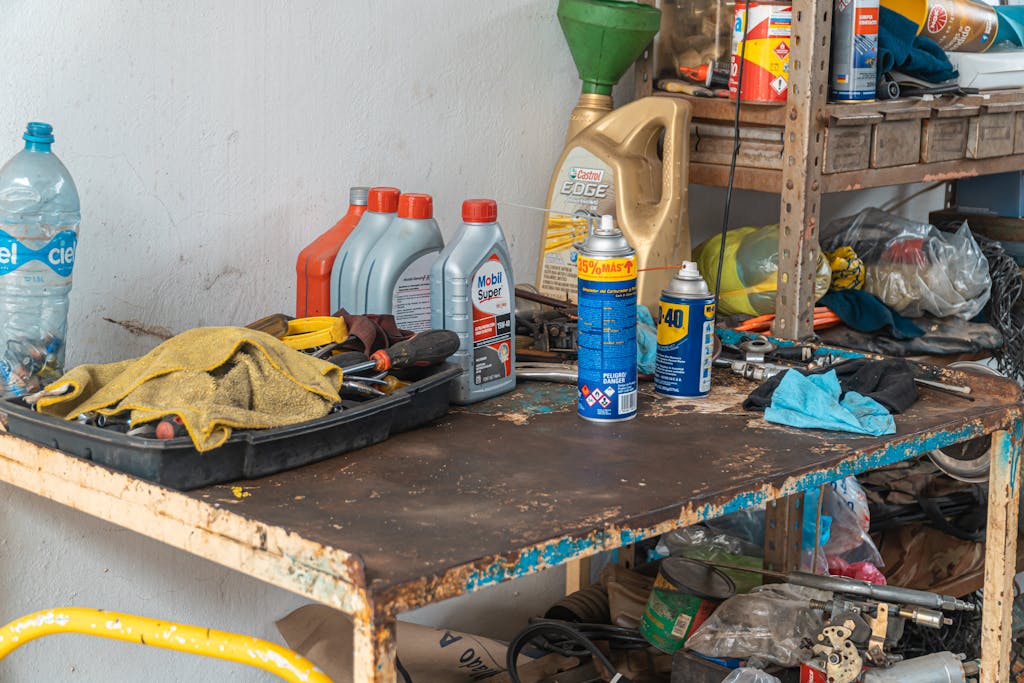 A cluttered workbench in an automobile garage with tools, oil cans, and maintenance products.