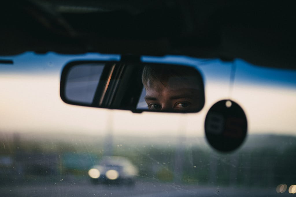 A thoughtful gaze captured in a car's rearview mirror, with twilight sky in the background.