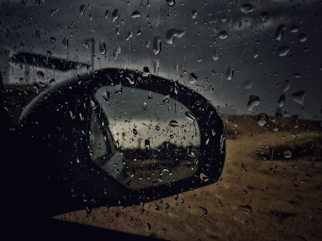 Close-up of a car side mirror with raindrops, capturing a wet and stormy atmosphere.