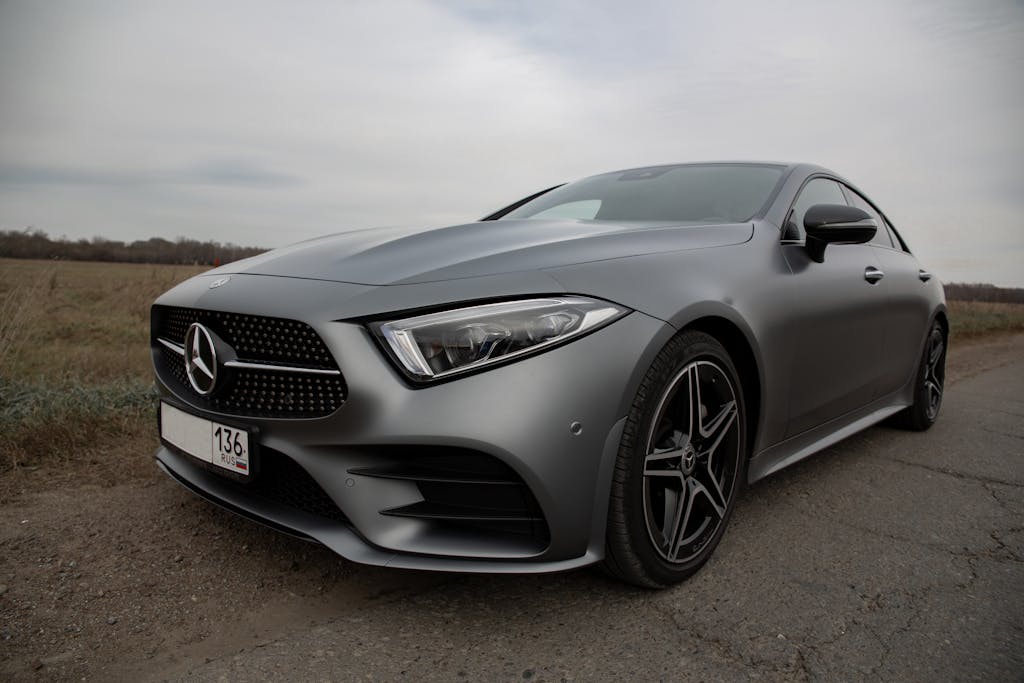 Luxury silver automobile with switched off headlight and tinted glass parked on roadside in rural area