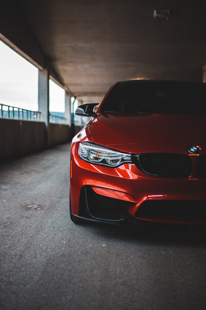 Parked red car with shiny headlights and tinted windshield on asphalt parking lot